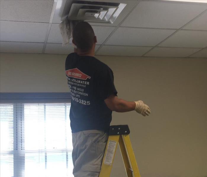  tech on ladder hand cleaning a metal-air register in the drop-ceiling