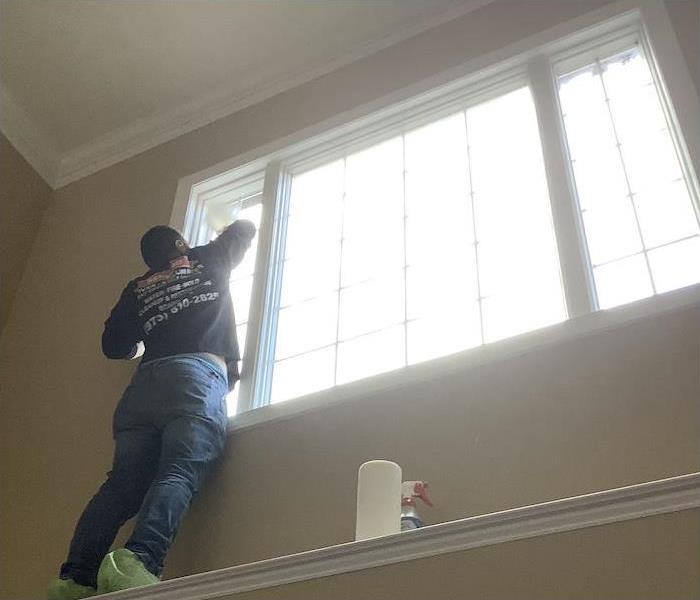 SERVPRO technicians cleaning away smoke damage on window and walls in a home